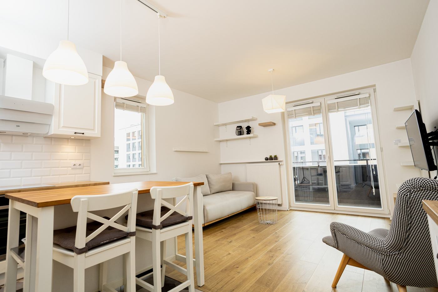 Rzeczywisty salon z białą kuchnią, drewnianą podłogą i wyjściem na balkon